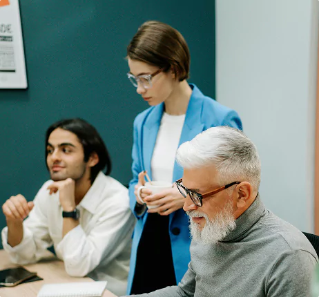 Three team members in a meeting, with an older man smiling while using a laptop and two younger colleagues listening attentively.