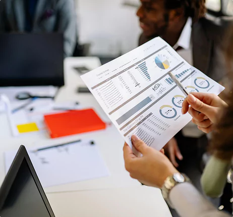 Hands holding a printed business report with charts and graphs during a team meeting.