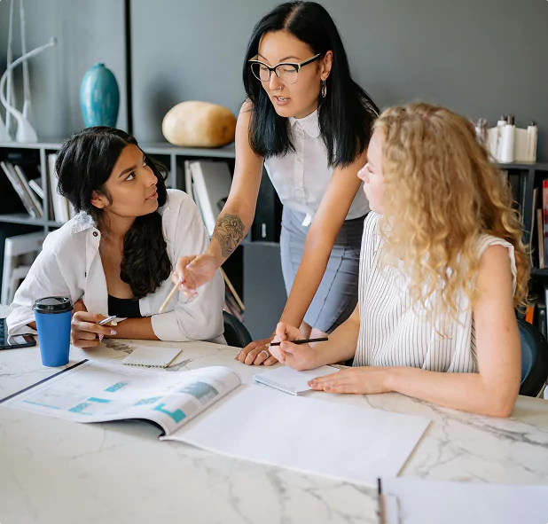 Three women collaborating on a project at a desk with open documents