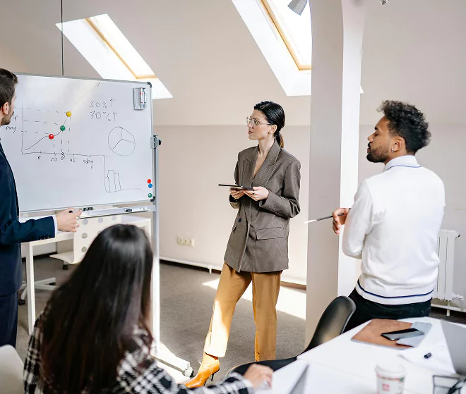 Colleagues analyzing data and charts on a whiteboard in a modern meeting room