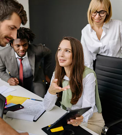 A group of four diverse professionals having a collaborative discussion around a desk with documents, a tablet, and a laptop.