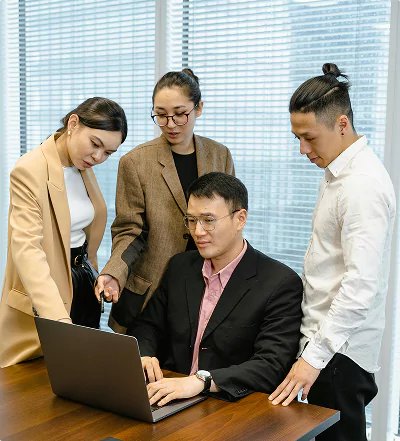 Four colleagues gathered around a laptop in a modern office.